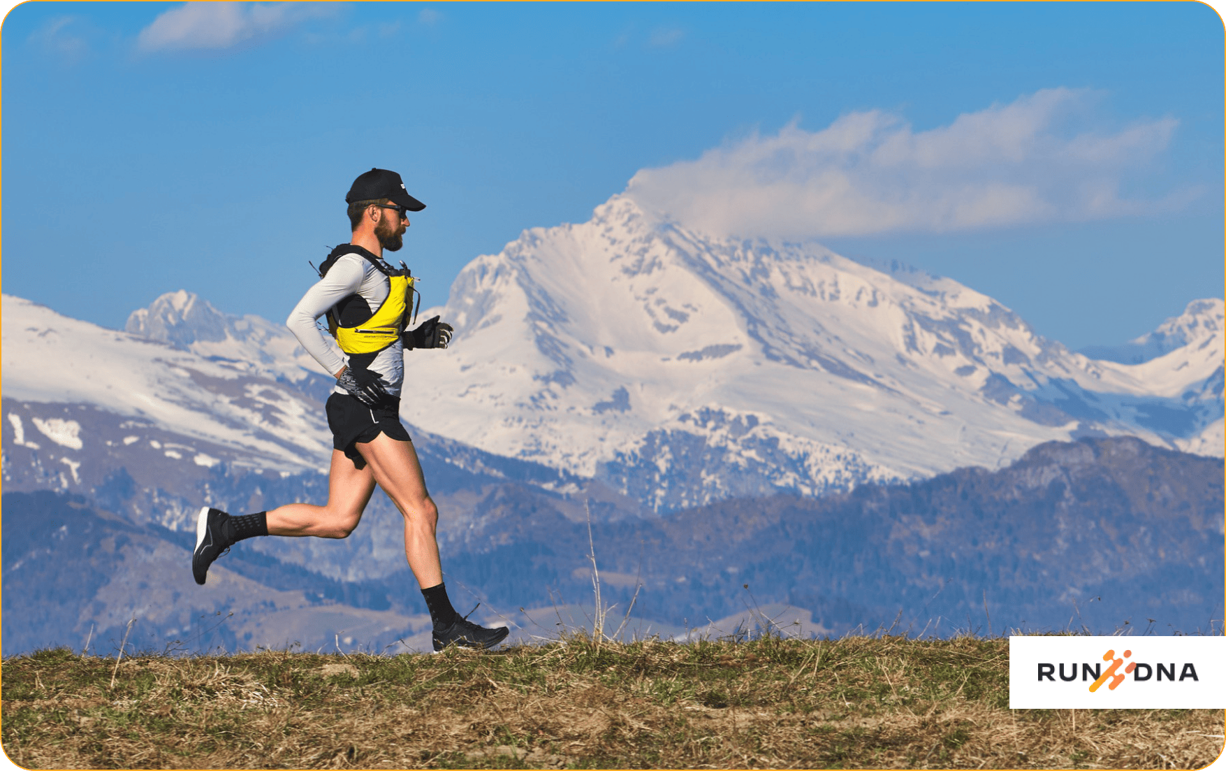 A man running on a trail with a stunning view of snow-covered mountains in the background. He is dressed in athletic gear suitable for the cold, while the icy white peaks and clear blue sky create a dramatic and serene backdrop.